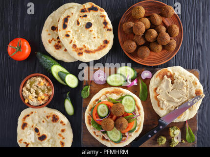 Falafels sul pan fritto pane pita con il piccante Hummus, pomodoro e fette di cetriolo. Ingredienti su sfondo, vista orizzontale dal di sopra Foto Stock