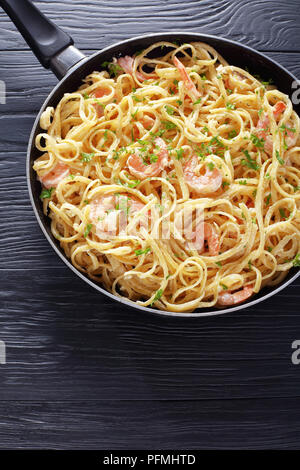 Deliziosi gamberetti cremosa Alfredo linguine cosparso con del prezzemolo tritato finemente in una padella su tavoli in legno nero, verticale vista da sopra, close-up Foto Stock
