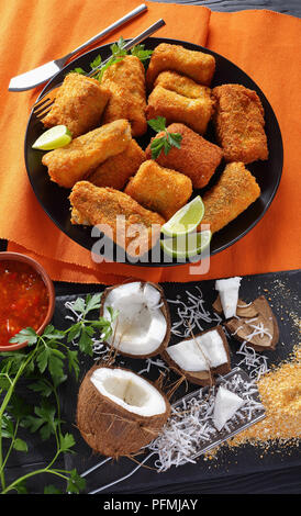 Deliziosi pezzi di croccante frittura di pesce rivestito con pane di noce di cocco grattugiato. cocco grattugiato e dolci fatti in salsa di mango nel recipiente a sfondo, vista da abov Foto Stock