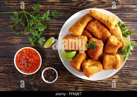 Deliziosi pezzi di croccante frittura di pesce rivestito in pastella di noce di cocco e briciole di pane sulla piastra bianca sul vecchio legno carbonizzate tabella, vista da sopra, close-up Foto Stock