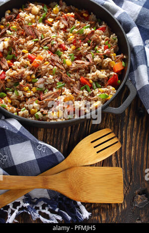 Un sottovaso - Carni bovine e di riso a grani lunghi con verdure, chicchi di mais e spezie in ghisa di PAN, di facile e rapida la ricetta, vista verticale da sopra Foto Stock