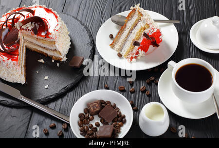 Porzione di deliziose torte con crema di formaggio servita mousse con tazza di caffè e crema. i chicchi di caffè e pezzi di cioccolato nero sul tavolo di legno, v Foto Stock