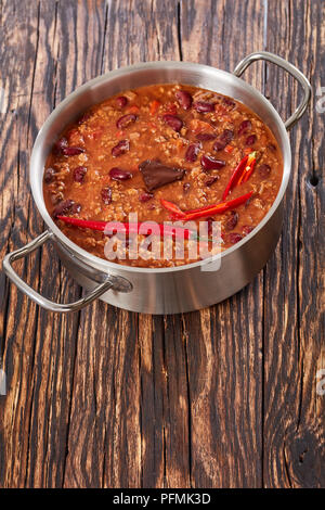 Una pentola di acqua calda deliziosa chili con carne con tutto il red hot chilis, fagioli, pomodori e pezzo di cioccolato, verticale vista da sopra Foto Stock