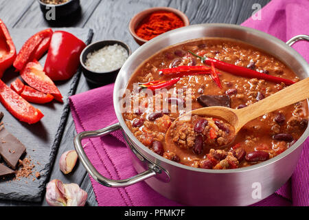 Deliziosi hot chili con carne con tutto il red hot chilis, fagioli, pomodori e pezzo di cioccolato in una pentola con ingredienti a sfondo, authen Foto Stock