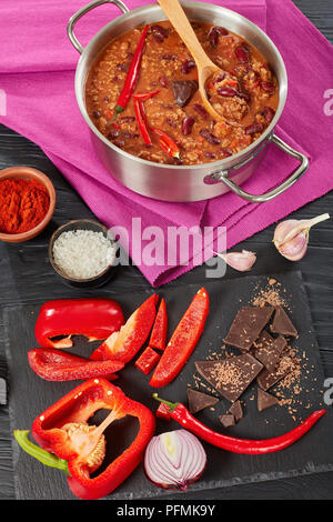 Deliziosi hot chili con carne con tutto il red hot chilis, fagioli, pomodori e pezzo di cioccolato in una pentola con ingredienti a sfondo, authen Foto Stock