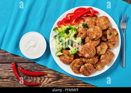 Cotte in forno succosa di pollo polpette di broccoli ripieni di formaggio grattugiato servito sulla piastra bianca con panna acida nella ciotola sul vecchio tavolo in legno, sano Foto Stock