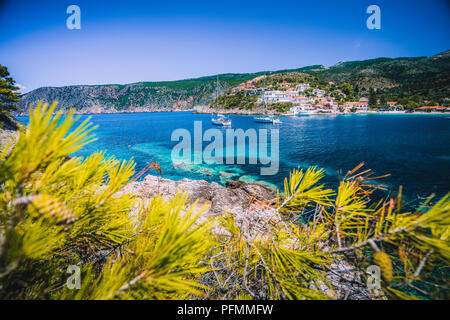 Incredibile Assos village, Cefalonia. La Grecia. Crociera bianco yachts soggiornando al di ancoraggio nel bellissimo verde smeraldo laguna colorata acqua. Incorniciato da alberi di pino Foto Stock