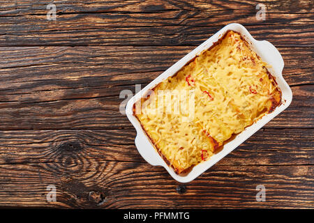 Deliziosi piatti fatti in casa a caldo enchiladas di tortilla di mais con Shredded carne, salsa, formaggio grattugiato e pezzi di chili in una teglia sul tavolo di legno, vista Foto Stock