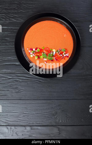 Gazpacho - in stile spagnolo estate freddo zuppa di pomodoro, cetriolo, pane e spezie in nero ciotola sul tavolo di legno, vista verticale dal di sopra, clos Foto Stock