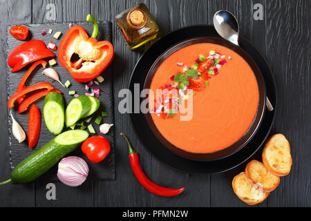 Porzione di deliziosa gazpacho nella ciotola nero - stile spagnolo estate freddo zuppa di pomodoro, cetriolo, pane, facile ricetta classica. Ingredienti su Foto Stock