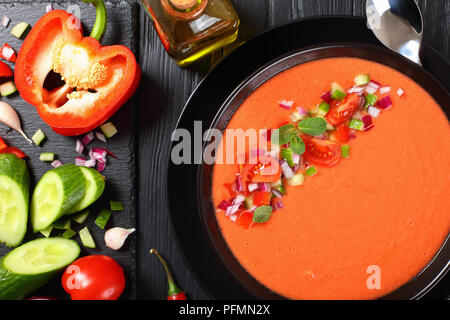 Porzione di deliziosa gazpacho nella ciotola nero - stile spagnolo estate freddo zuppa di pomodoro, cetriolo, pane, ricetta classica. Ingredienti su woode Foto Stock