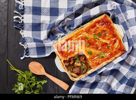 Deliziose Carni bovine e torta di Funghi Conditi con crosta dorata sfoglia di pasta sfoglia in una teglia sul tavolo di legno con carta asciugatutto, ricetta australiana, vie Foto Stock