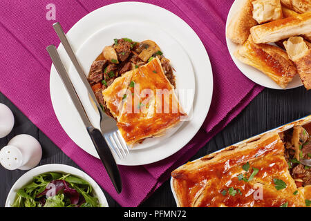 Appena sfornato carne australiana e torta di Funghi Conditi con crosta dorata sfoglia di pasta sfoglia in una teglia e pezzo di torta servita su una piastra con taglio Foto Stock