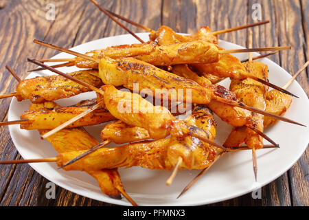 Delizioso pollo satay su spiedini su una piastra bianca sul tavolo di legno, ricetta classica, vista da sopra, close-up Foto Stock