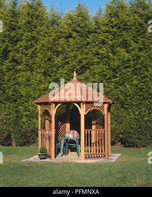 Gazebo in legno con pannelli da traforo, contenenti mobili da giardino, impostare nella parte anteriore di alberi di alto fusto. Foto Stock