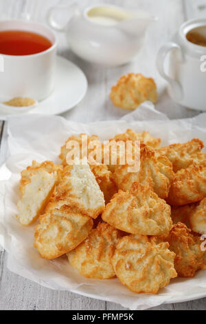 Deliziosa casa amaretti di cocco i cookie su una piastra bianca sul tavolo di legno con la tazza di tè e caffè, zuccheriera e panna fresca in un bricco per il latte a sfondo, Foto Stock