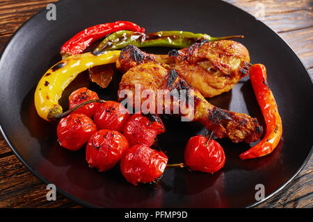 Porzione di pollo grigliato con bacchette varicolored il peperoncino e i pomodori ciliegia servito su una piastra nera, vista orizzontale dal di sopra, close-up Foto Stock