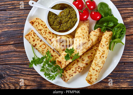 Fritto delizioso frittelle sottili o Crepes ripiene di carne di pollo servito su una piastra bianca con spinaci, pomodorini e salsa fatta in casa il pesto, vista Foto Stock