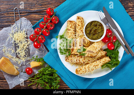 Fritto delizioso Crepes ripiene di carne di pollo cosparsi di parmigiano grattugiato, servita su una piastra bianca con spinaci, pomodorini e home Foto Stock