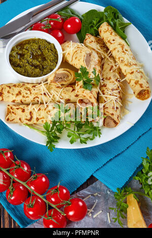 Crepes ripiene di carne di pollo cosparsi di parmigiano grattugiato, servita su una piastra bianca con spinaci, pomodorini e salsa fatta in casa il pesto Foto Stock