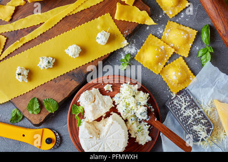 La cottura fino deliziosi ravioli con ripieno di ricotta ripieno di formaggio mescolato con un trito di menta e foglie di basilico su un concreto tavolo da cucina con ingredienti, Foto Stock