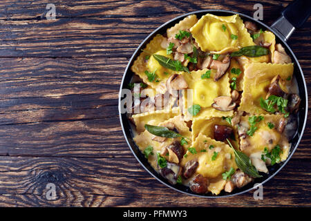 Deliziosi ravioli ripieni di ricotta cotti in aglio cremosa salsa di funghi in una padella su un vecchio tavolo di legno, vista da sopra, copia spac Foto Stock