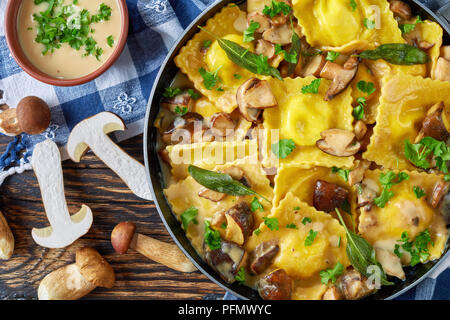 Ravioli fatti in casa ripieni di ricotta cotti in aglio cremosa salsa di funghi in una padella su un vecchio tavolo di legno con carta asciugatutto e fresco Foto Stock