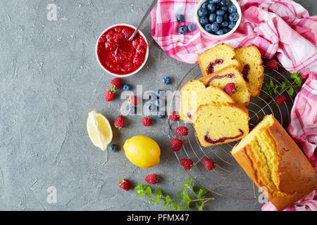 Limone ciambellone con marmellata di frutti di bosco di riempimento noto anche come gateau de voyage la torta su un tavolo in cemento con gli ingredienti della cucina francese, vista da sopra, c Foto Stock