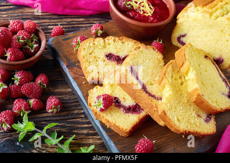 Close-up di limone ciambellone con confettura di lamponi riempimento su un tagliere un vecchio tavolo di legno con frutti di bosco freschi, scuro in stile rustico, cucina francese, Foto Stock