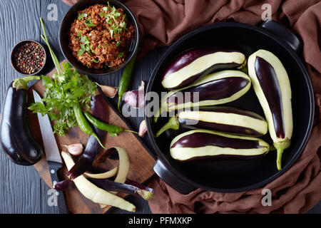 Cucina di melanzane ripiene, melanzane con massa di carne di manzo, pomodori e cipolle. ingredienti su di un tavolo di legno, vista da sopra, laici piatta Foto Stock