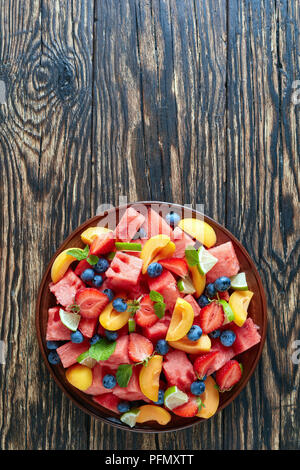 Deliziosa colorato anguria fresca insalata con mirtilli, pesche tagliate a fette, fragola e calce su una piastra di argilla su un vecchio tavolo rustico, vista verticale fr Foto Stock