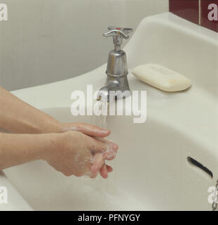 Lavarsi le mani sotto acqua corrente, bianco saponetta sul bordo del bacino, vicino. Foto Stock