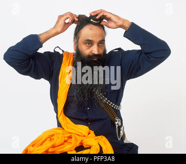 L'uomo posizionando il tessuto di base in posizione sulla sua testa, turban arancione tela sospesa sopra la sua spalla Foto Stock