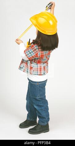 Ragazza vestita come un costruttore di contenimento del nastro di misurazione, guardando lontano Foto Stock