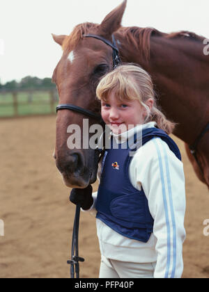 Ragazza in piedi accanto al marrone scuro pony, tenendo redini. Foto Stock