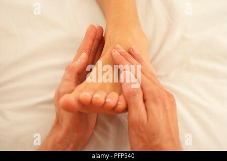 Mani dell'uomo massaggiando delicatamente una donna di piede, close-up Foto Stock