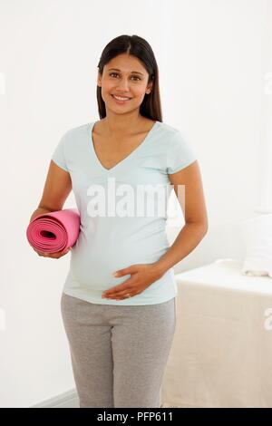 Giovane donna incinta holding arrotolato tappetino rosa Foto Stock