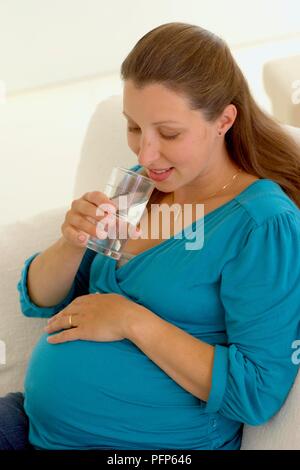 Donna incinta di bere un bicchiere di acqua Foto Stock