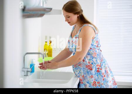 Donna incinta in fiore abito modello di lavaggio delle mani, vista laterale Foto Stock