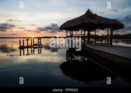 Sun impostazione nella calma laguna dietro Utila segno e dock, Utila, Honduras, America Centrale Foto Stock