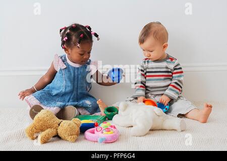 13 mesi bambina e 10 mesi bambino seduto sul pavimento a giocare con i giocattoli Foto Stock