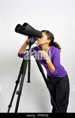 Giovane donna guardando attraverso la coppia di elevata potenza binocolo su treppiede Foto Stock