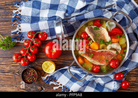 Sostanziosa zuppa di pesce - greco psarosoupa in una casseruola di metallo su un vecchio tavolo rustico con siviera, pomodori, grani di pepe e di asciugatutto, vista da sopra, Foto Stock