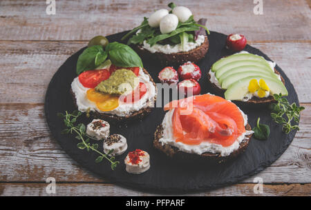 Crostino con salmone, avocado, mozzarella, pomodoro, pesto,olive, crema di formaggio. Mix di diversi spuntini e stuzzichini Foto Stock