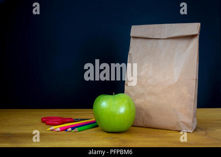 Pranzo a scuola. Sacchetto di carta e una mela verde sulla parte superiore del banco in legno Foto Stock