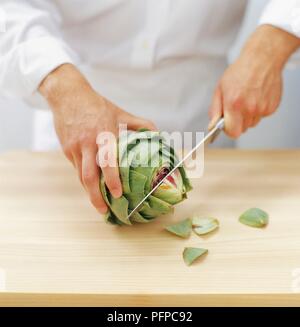 Chef usando coltello da cucina per tagliare la punta di carciofi sul tagliere di legno Foto Stock