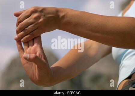 Giovane donna stretching prima di arrampicata, tirando indietro le dita della mano destra con la mano sinistra, close-up Foto Stock