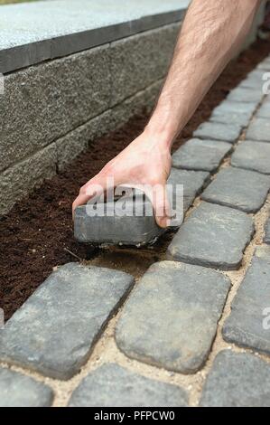 L'uomo rimozione blocco dal percorso di mattoni per formare la piantagione pocket, close-up Foto Stock