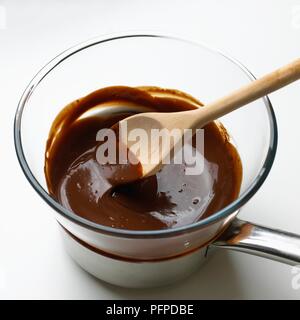 Il cucchiaio di legno nel cioccolato fuso nel recipiente di miscelazione sulla parte superiore della pentola Foto Stock