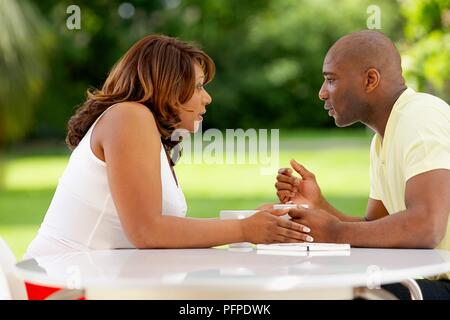 Giovane seduto al tavolo esterno, parlando Foto Stock